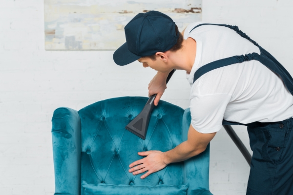 sillón reclinable; un hombre con overol limpiando un sillón con aspiradora